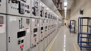 Long row of control panels in an industrial electrical control room, well-lit and spacious.